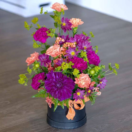 Vibrant artificial flower bouquet rental with pink dahlias purple hydrangeas and orange roses in elegant black vase for gala dinner centerpieces