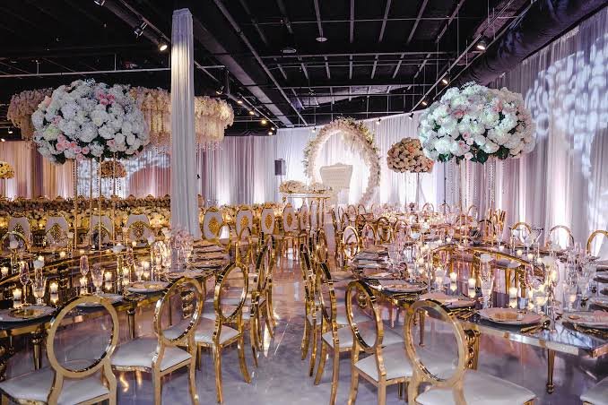 Elegant gold dior chairs with white floral centerpieces under chandeliers engagement party Riyadh